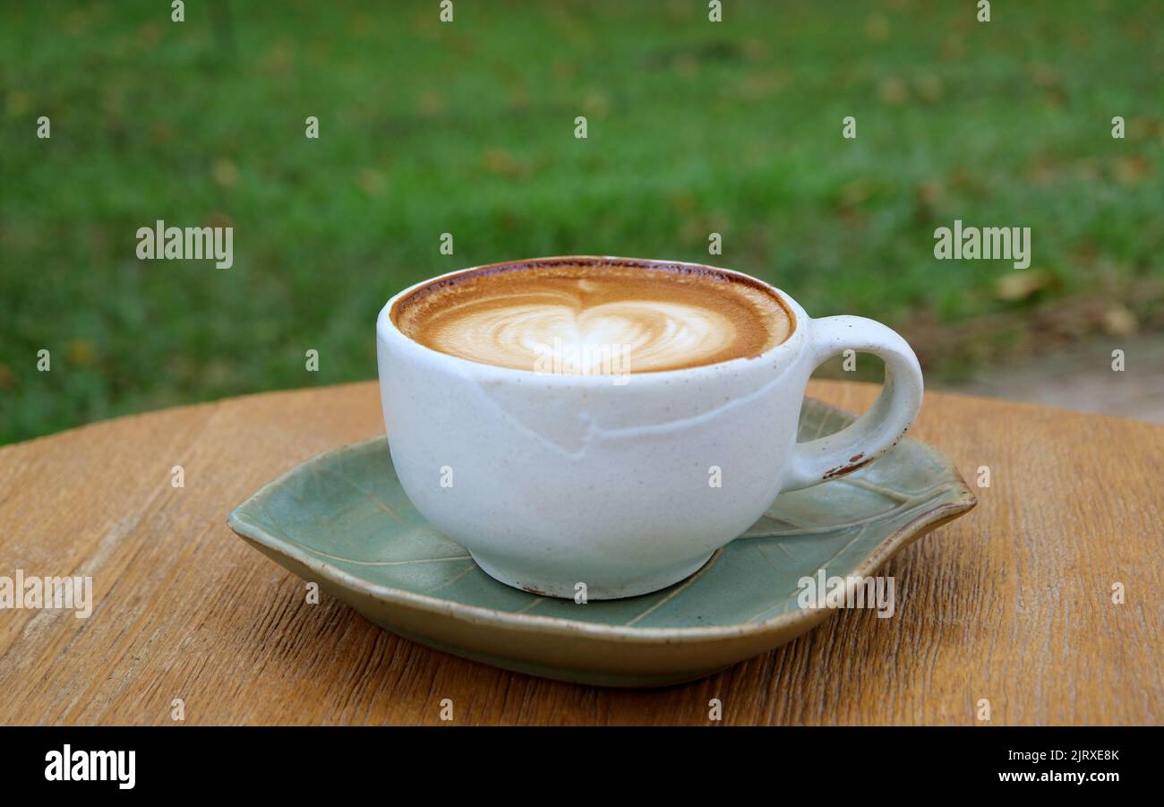 Eine Tasse Cappuccino-Kaffee mit herzförmiger Latte-Kunst isoliert auf einem Holztisch Stockfoto