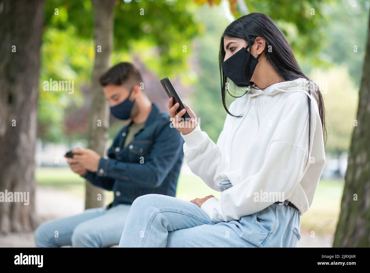 Maskierte Personen, die während einer Coronavirus-Pandemie ein Mobiltelefon im Park benutzten Stockfoto