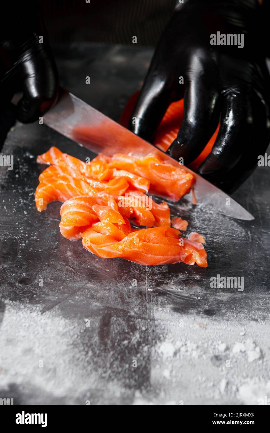 Nahaufnahme des Küchenchefs, der zum Kochen von frischem Lachsfilet auf schwarzem Hintergrund zubereitet wurde. Roher Fisch auf dem Eisblock Stockfoto