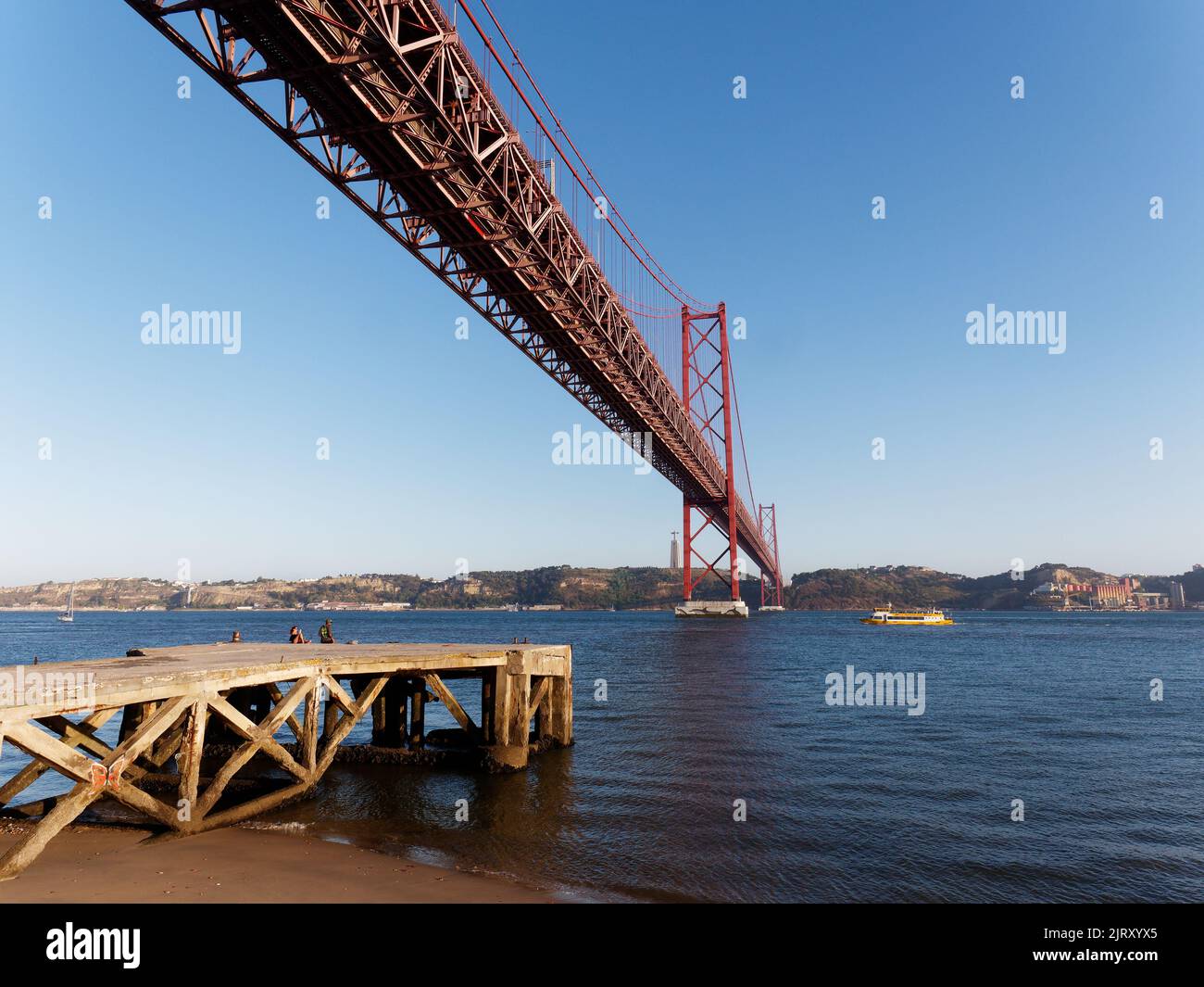 Ponte 25 de Abril (Brücke vom 25. April) über den Fluss Tejo in Lissabon, Portugal. Anlegestelle und Strand links. Stockfoto