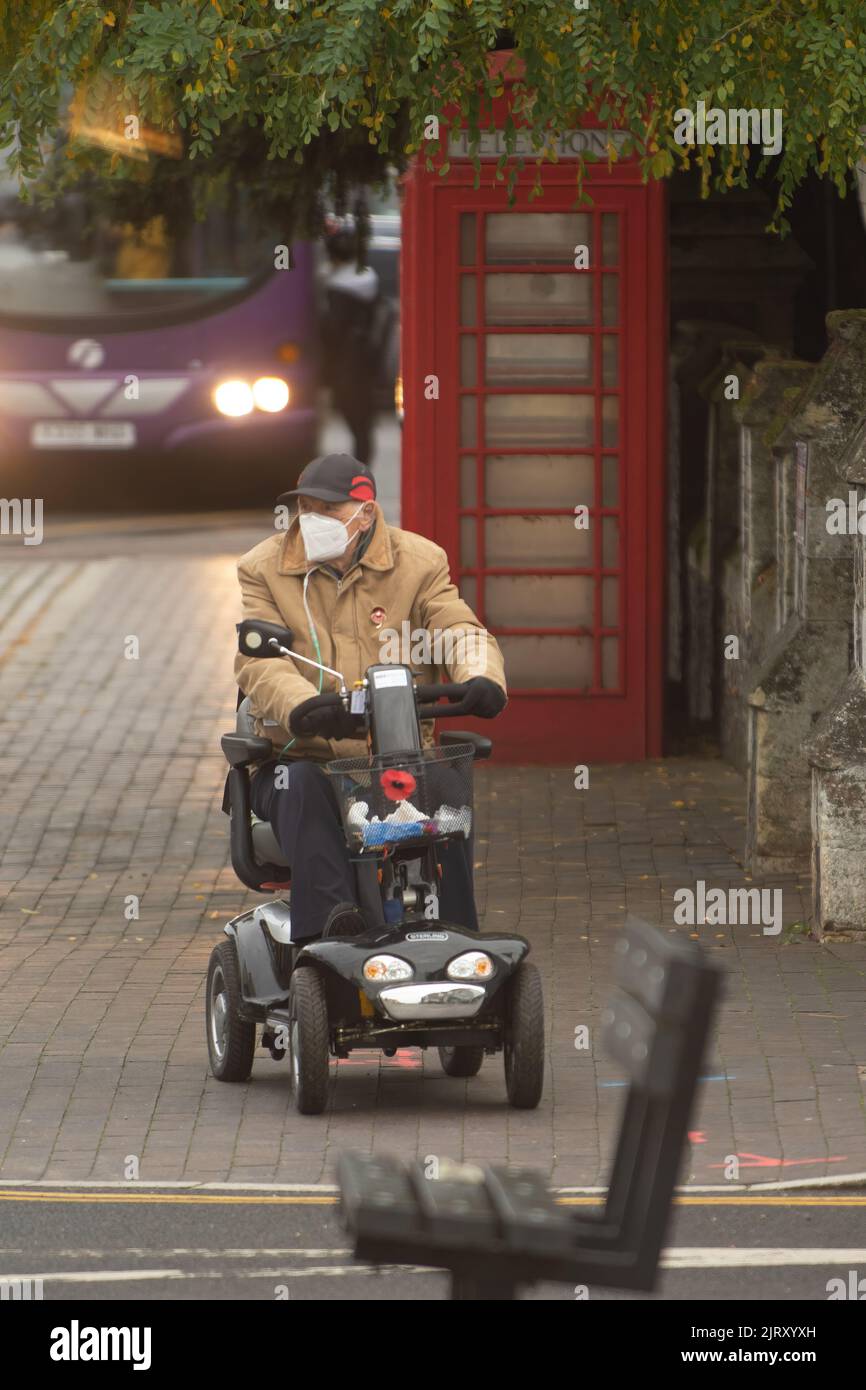 Eine vertikale Aufnahme eines alten Mannes mit Gesichtsmaske auf einem Mobilitätsroller auf der Straße Stockfoto