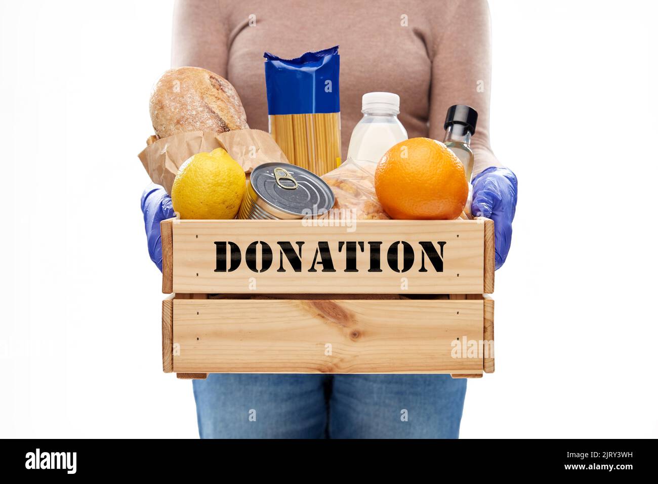 Frau in Handschuhen mit Lebensmittelspende in Holzkiste Stockfoto