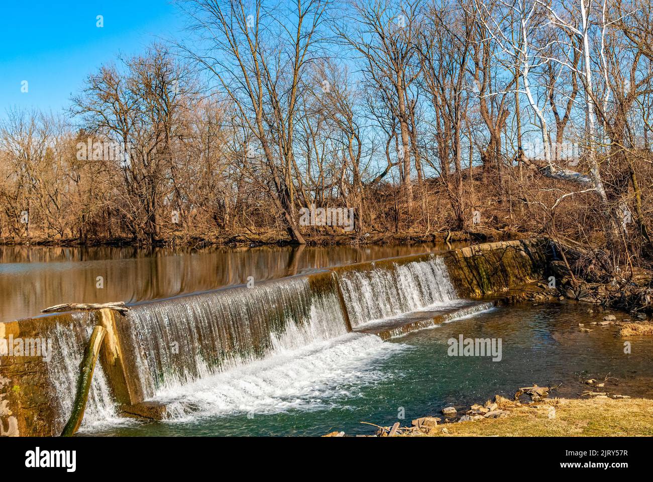 Ein Blick auf einen von Menschen gemachten Damm und Wasserfall, der an einem sonnigen Wintertag auf dem Land gefunden wurde Stockfoto
