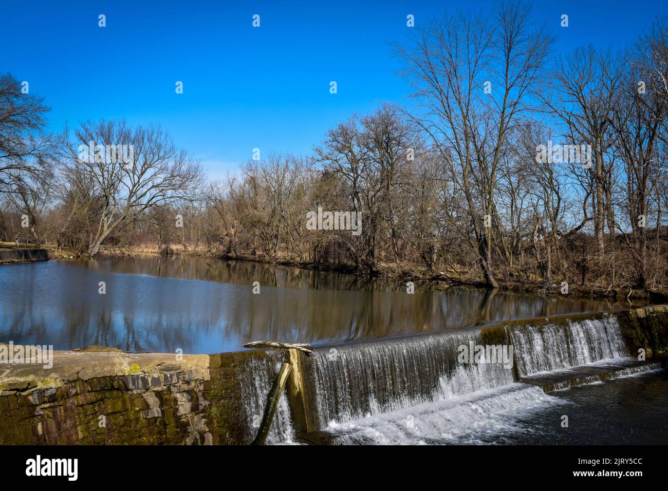 Ein Blick auf einen von Menschen gemachten Damm und Wasserfall, der an einem sonnigen Wintertag auf dem Land gefunden wurde Stockfoto