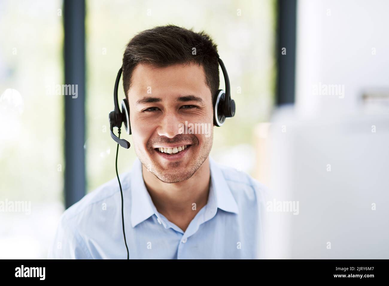 Hallo. Du kommst durch zu. Porträt eines glücklichen jungen Mannes, der ein Headset trägt und bei der Arbeit einen Computer benutzt. Stockfoto
