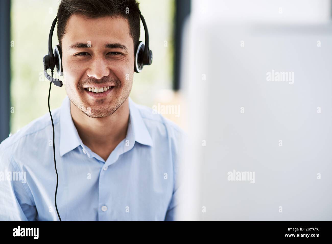 Kundenservice ist meine Priorität. Porträt eines glücklichen jungen Mannes, der ein Headset trägt und bei der Arbeit einen Computer benutzt. Stockfoto