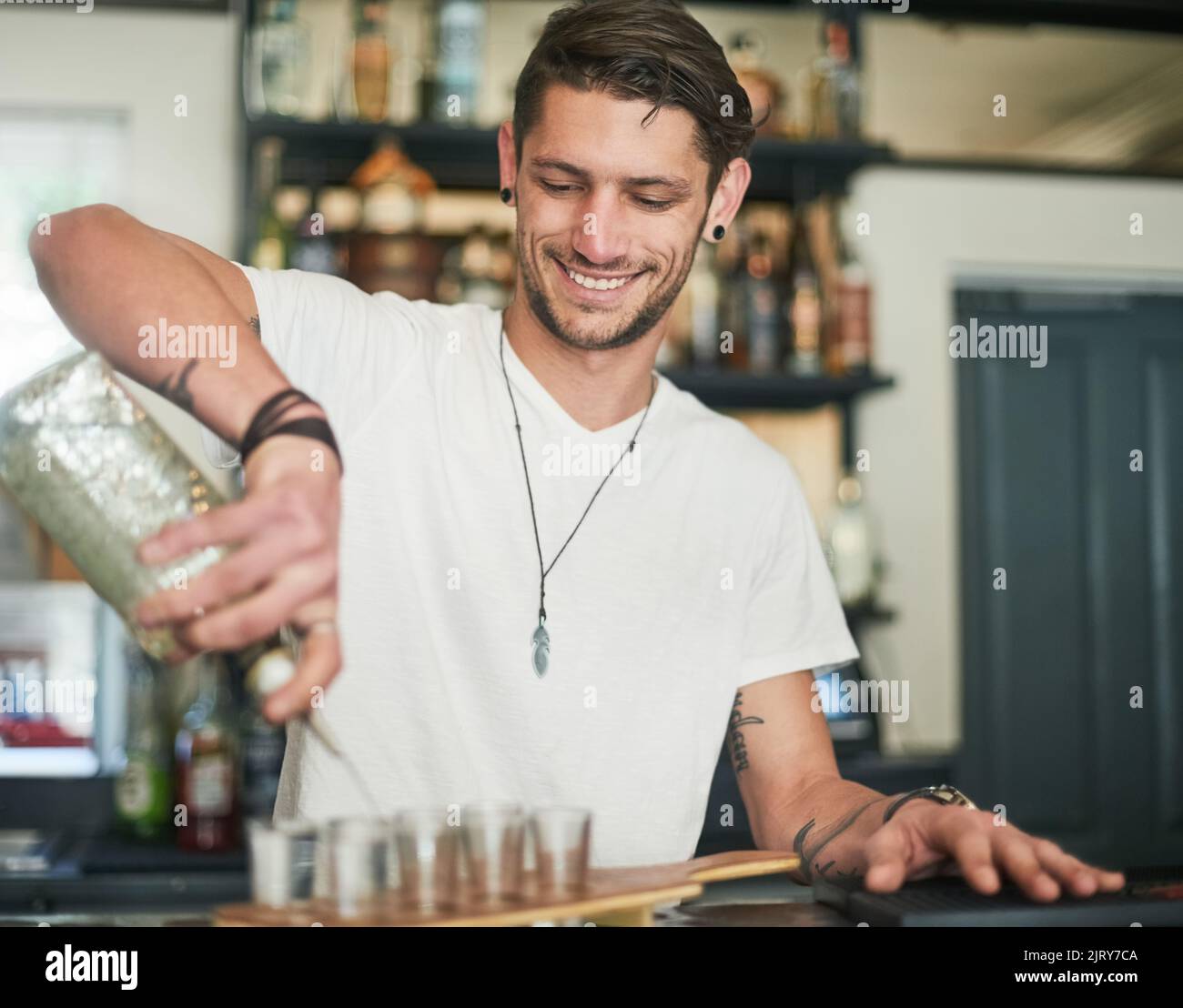 Ein glücklicher junger Barkeeper gießt Schüsse hinter die Bar. Stockfoto