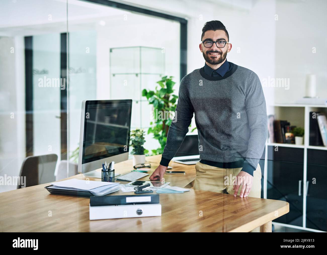 Die harte Arbeit zahlt sich schließlich aus. Porträt eines selbstbewussten jungen Designers, der an seinem Schreibtisch in einem Büro steht. Stockfoto