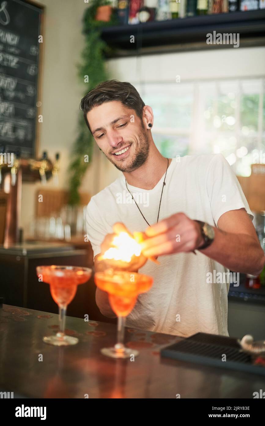 Was ist das Leben ohne ein wenig Flair. Ein fröhlicher junger Barkeeper zündet hinter der Bar einen Cocktail an. Stockfoto