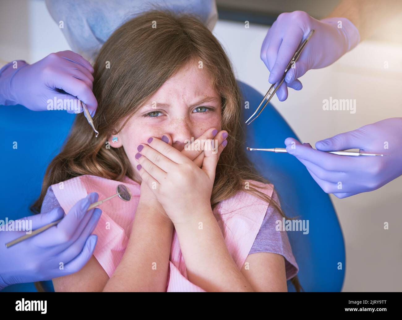 Zahnarztbesuche können beängstigend sein. Ein kleines Mädchen, das erschrocken aussieht, als Zahnärzte sich bereit machen, sie zu untersuchen. Stockfoto