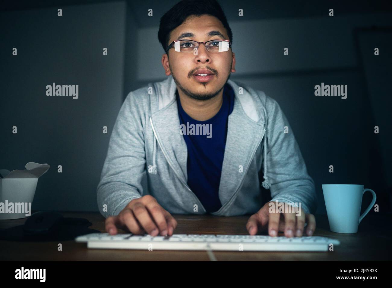 Codierung bis spät in die Nacht. Ein junger Mann, der spät in der Nacht an seinem Computer arbeitet. Stockfoto