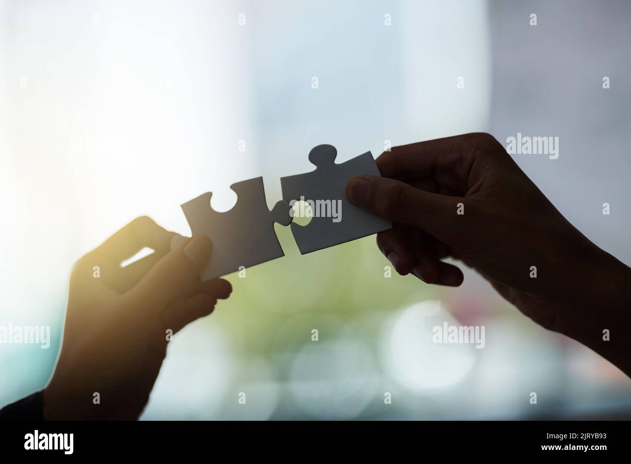 Einige Dinge passen einfach zusammen. Zwei silhouettierte Hände halten Puzzleteile an einem Fenster. Stockfoto