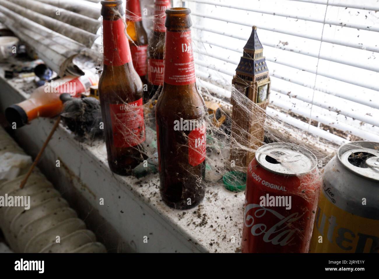 Spinnweben und tote Käfer sammeln sich auf leeren Bierflaschen und Dosen auf einer Fensterbank. Dieses Gebäude wurde seitdem abgerissen. Stockfoto