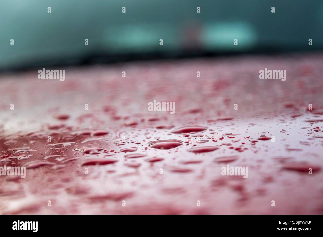 Spritzer und Wassertropfen auf einer roten Autooberfläche bilden einen wunderschönen Hintergrund mit Texturmustern und einigen Teilen im Fokus. Stockfoto