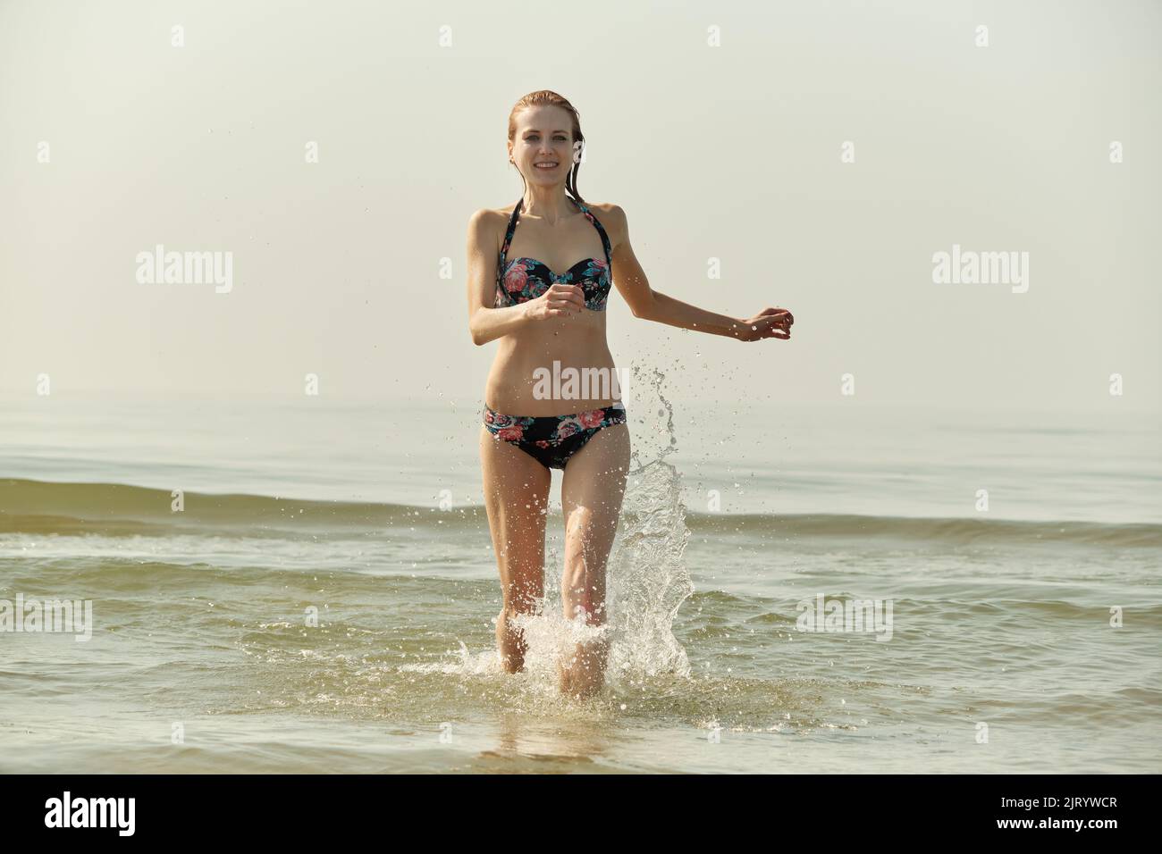 Single glücklich junge blonde Haare Frau im Bikini läuft auf See surfen mit Spritzern Stockfoto