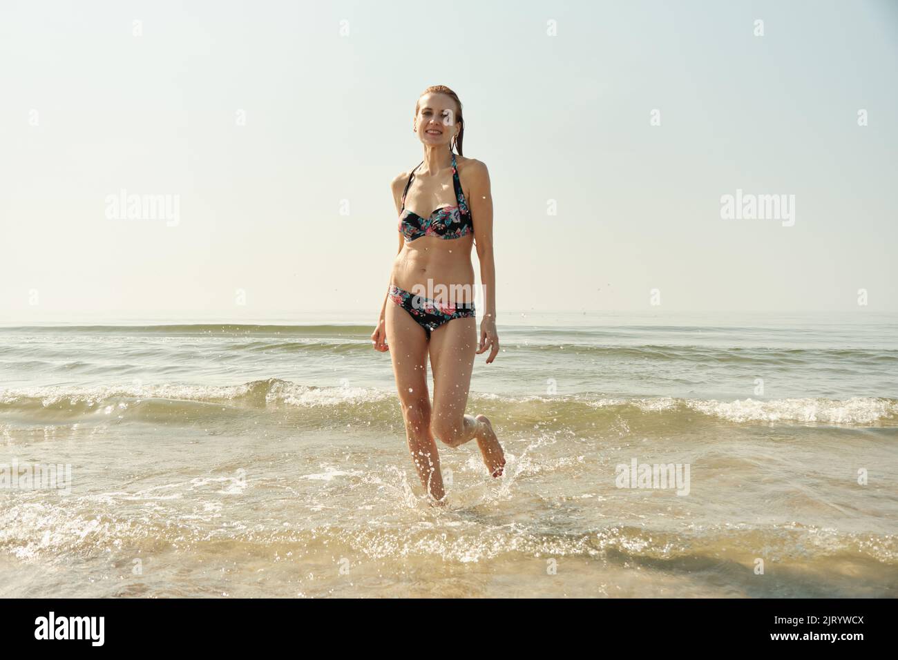 Single glücklich junge blonde Haare Frau im Bikini läuft auf See surfen mit Spritzern Stockfoto