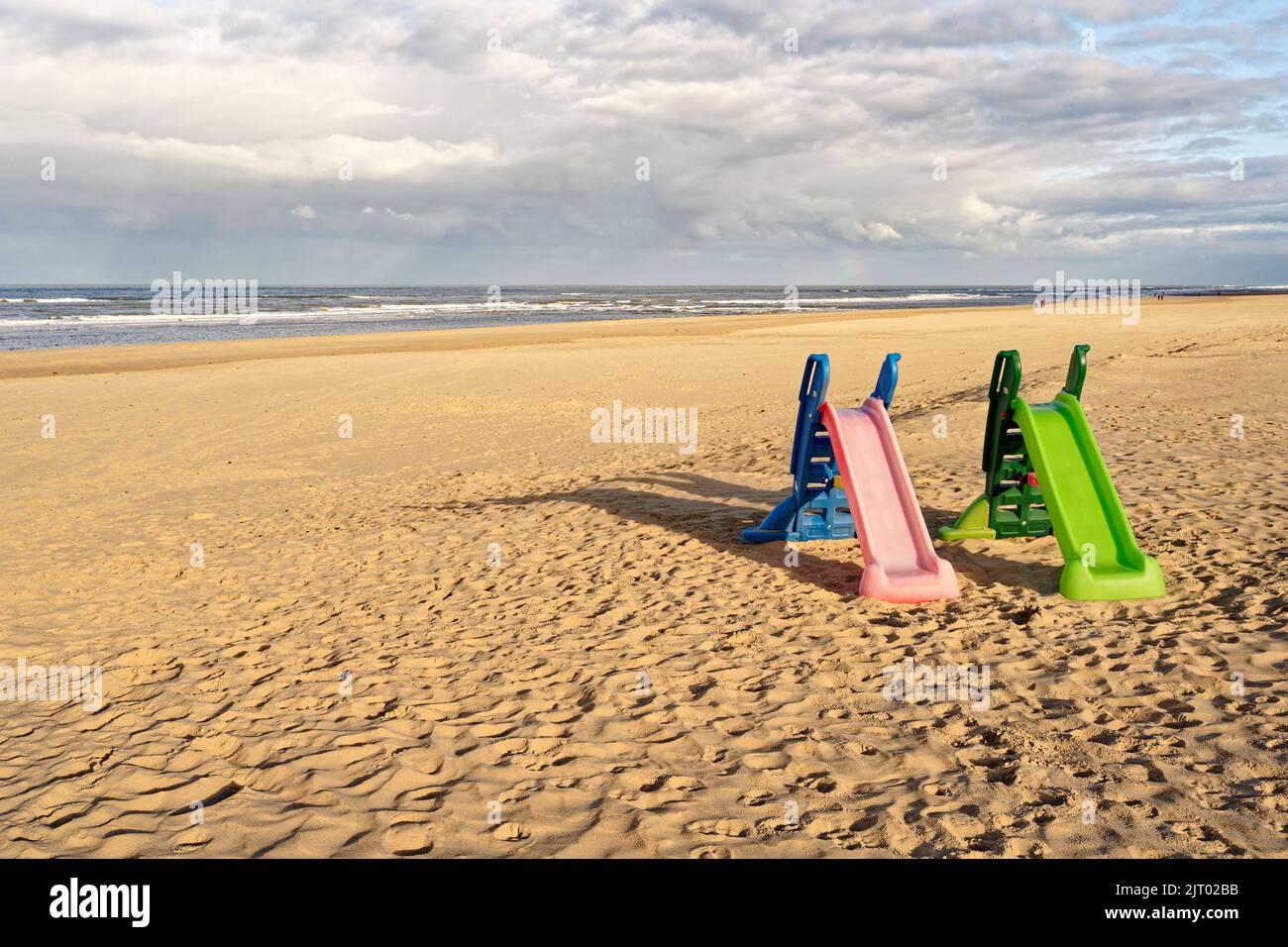 Zwei Spielplatzrutschen an einem fast leeren Strand, eine grüne und eine rosa. Nordholland Dünenreservat, Egmond aan Zee, Niederlande. Stockfoto