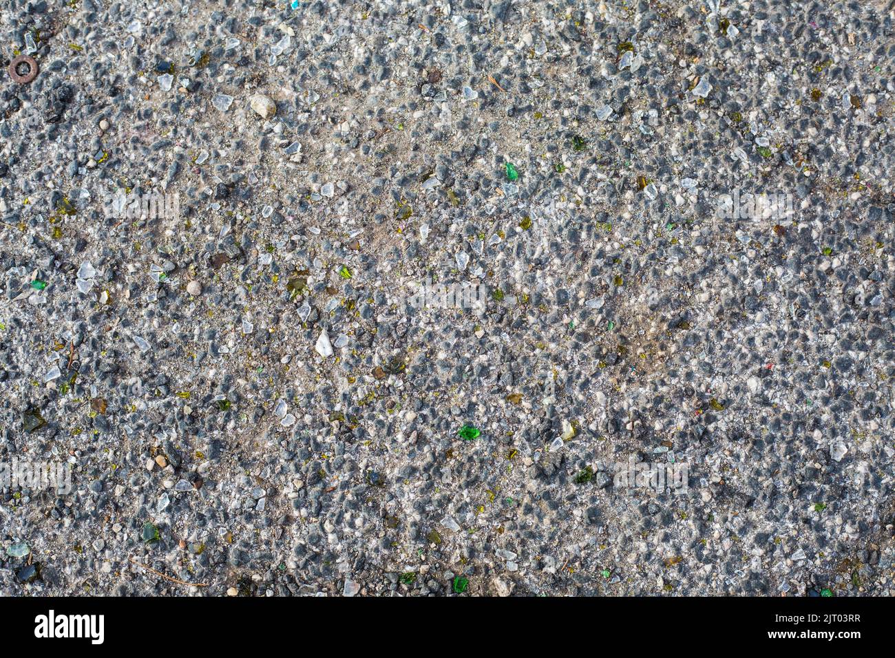 Hintergrund von altem Asphalt. Graue Straßenoberfläche mit kleinen Felsen und grünen Stücken aus gebrochenem Glas. Stockfoto