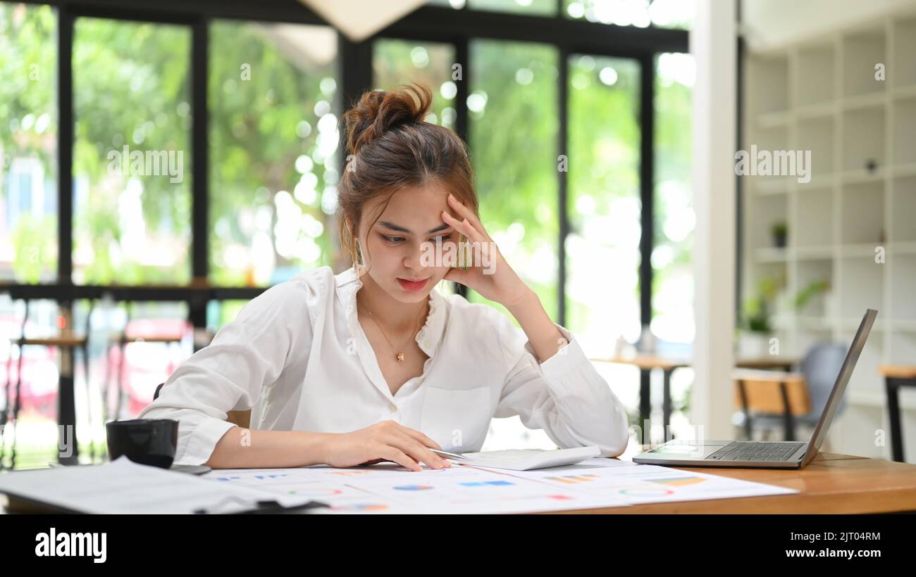 Müde Geschäftsfrau, die ihren Kopf hält und das Dokument liest. Konzept für emotionalen Druck, Stress am Arbeitsplatz Stockfoto