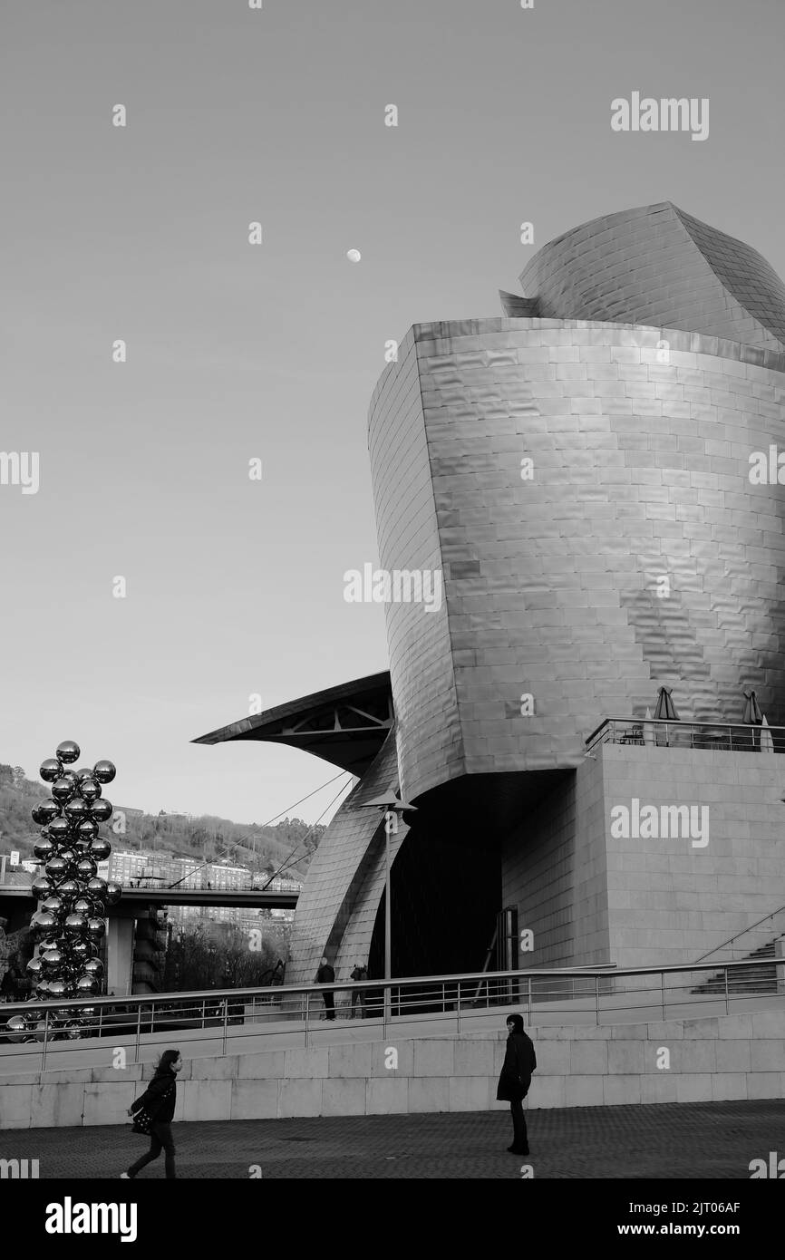 Eine vertikale Aufnahme des Guggenheim Museum Bilbao in Schwarz-Weiß mit dem Mond im Hintergrund Stockfoto