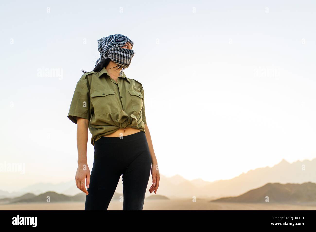 Frau mit verdecktem Kopf und Gesicht mit schwarz-weiß kariertem Schal stehen Wüste Hintergrund Stockfoto