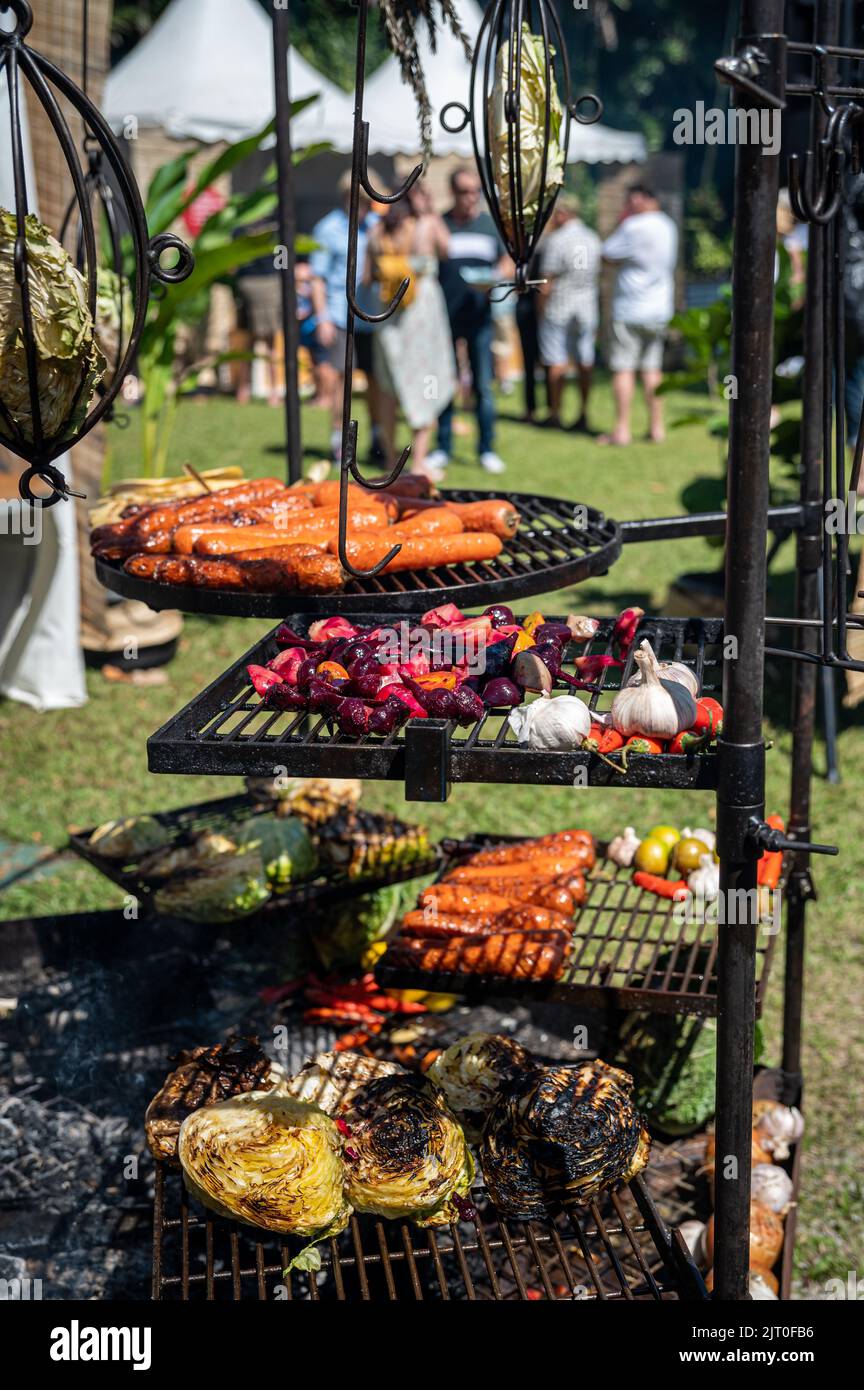 Aufwendige Grillstruktur im Vordergrund, die gemischtes Gemüse röstet, während sich die Gäste im Hintergrund bei einem Festival in Port Douglas, Australien, mischen. Stockfoto