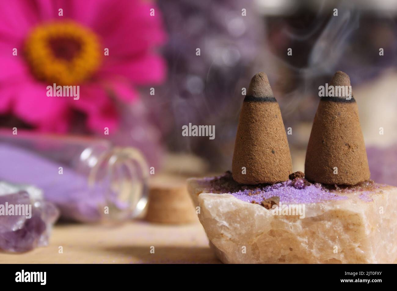 Amethyst-Kristalle mit Blumen und Räucherkegel auf Meditationstisch Stockfoto