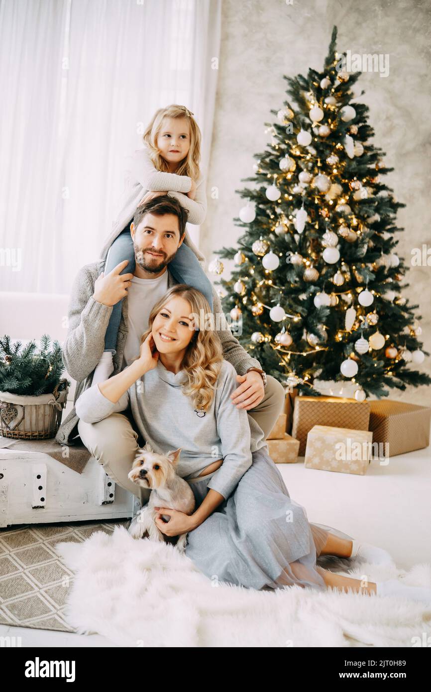 Glückliche Familie: Mama, Papa und Haustier. Familie in einem hellen Neujahrsraum mit einem Weihnachtsbaum. Stockfoto