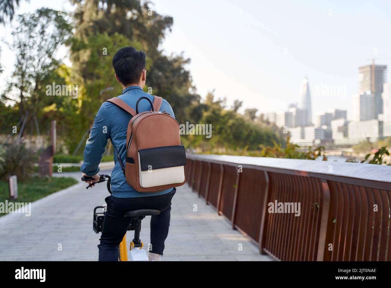 Rückansicht eines asiatischen jungen erwachsenen Mannes, der im Stadtpark Fahrrad reitet Stockfoto