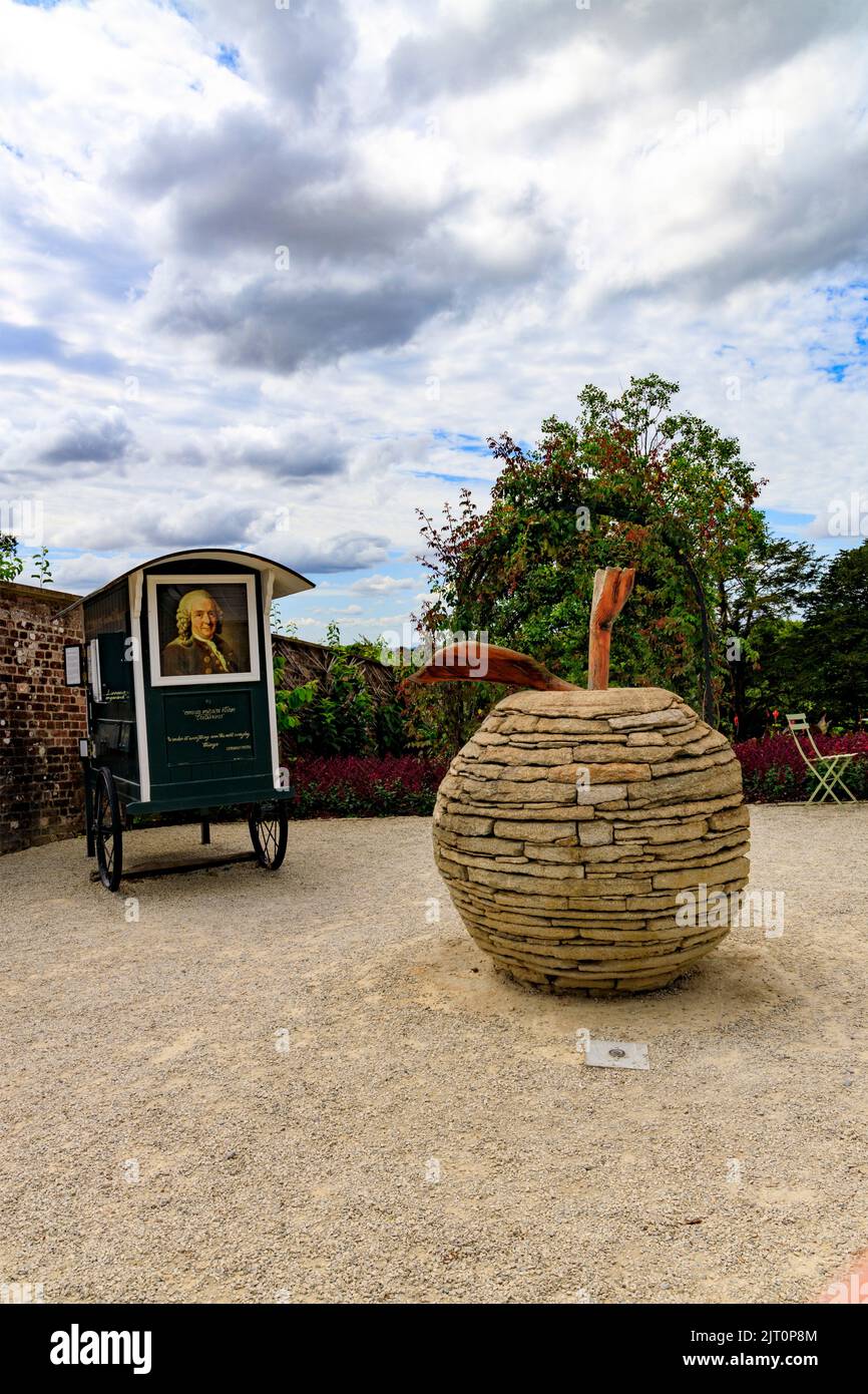 Ein Stein-Apfel-Kunstwerk und ein mobiler Carl Linnäus (schwedischer Botaniker und Taxonom) sind im Garten „The Newt in Somerset“, bei Bruton, England, Großbritannien, ausgestellt Stockfoto