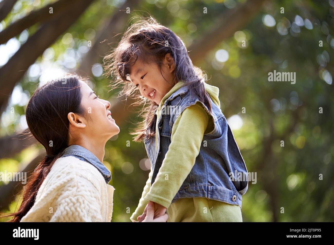Junge asiatische Mutter sitzt auf Gras im Park mit einem angenehmen Gespräch mit niedlichen Tochter Stockfoto
