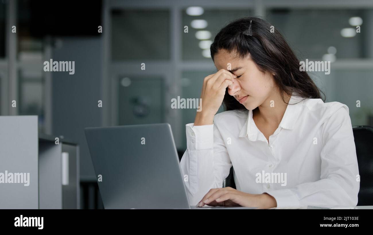 Junge gestresste müde überarbeitete weibliche Büroangestellte, die an einem Laptop mit Augenermüdungsmassagen arbeitet, fühlt sich Nasenrücken angespannt Kopfschmerzen an Stockfoto