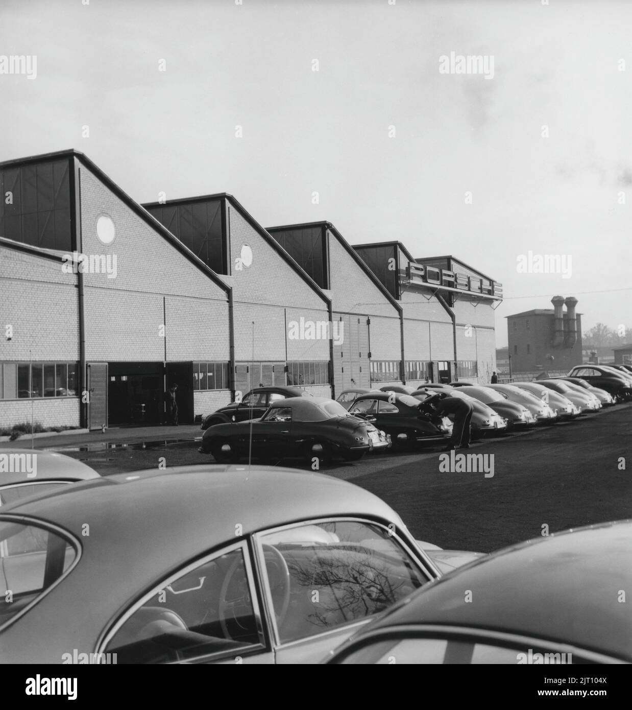 Porsche Geschichte. Eine seltene Ansicht der Porsche-Autofabrik in Stuttgart Deutschland im Jahr 1950s. Auf dem Werksgelände sind Porsche-Fahrzeuge in verschiedenen Produktionsstufen zu sehen. Das Emblem von Porsche ist auf dem Fabrikgebäude zu sehen. 1951. Stockfoto