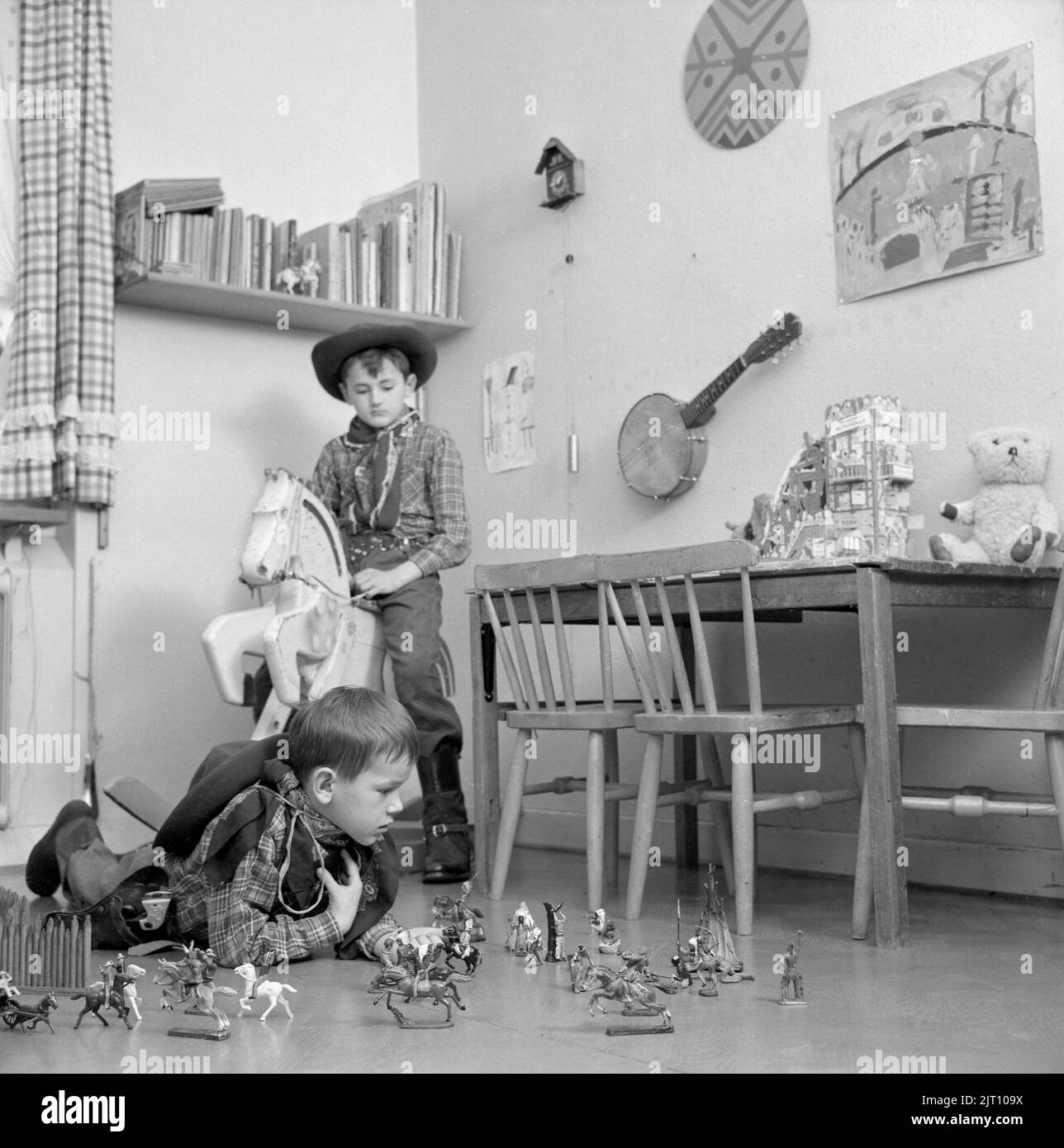 Jungen in den 1950s. Zwei Jungen in ihrem Spielzimmer sind als Cowboys gekleidet. Einer reitet auf einem Holzpferd und einer spielt auf dem Boden mit Figuren von Cowboys und indianern. Schweden 1953 Conard Ref. 2273 Stockfoto