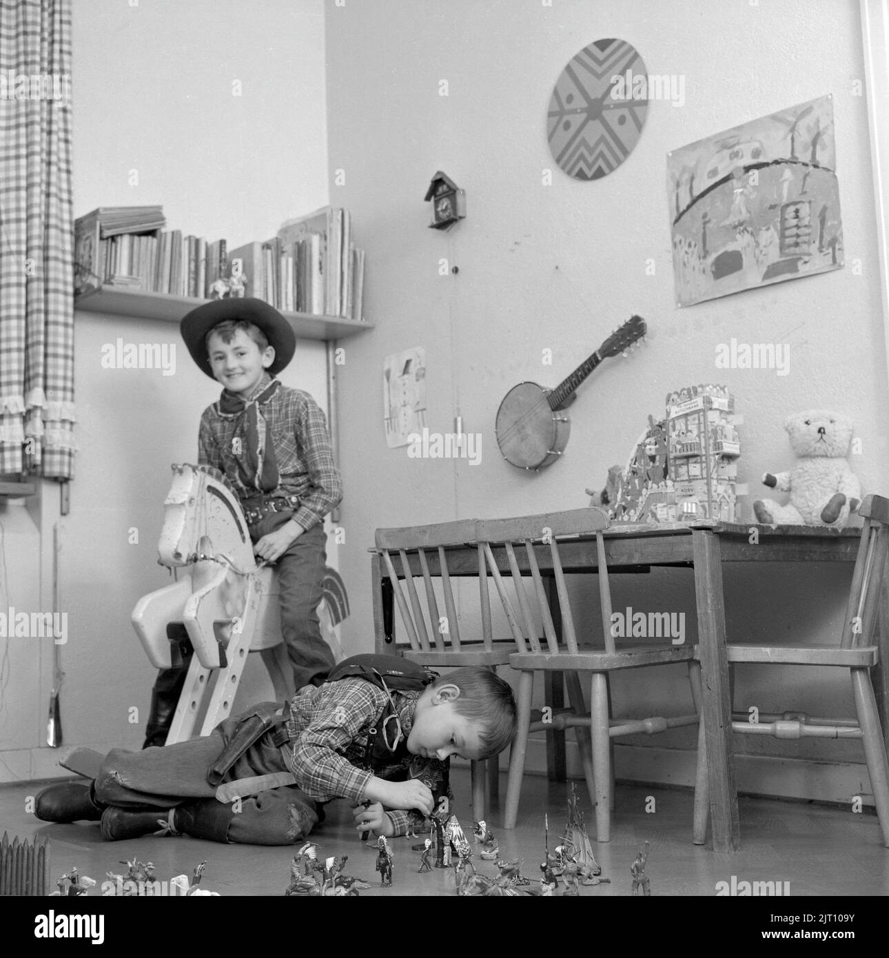 Jungen in den 1950s. Zwei Jungen in ihrem Spielzimmer sind als Cowboys gekleidet. Einer reitet auf einem Holzpferd und einer spielt auf dem Boden mit Figuren von Cowboys und indianern. Schweden 1953 Conard Ref. 2273 Stockfoto