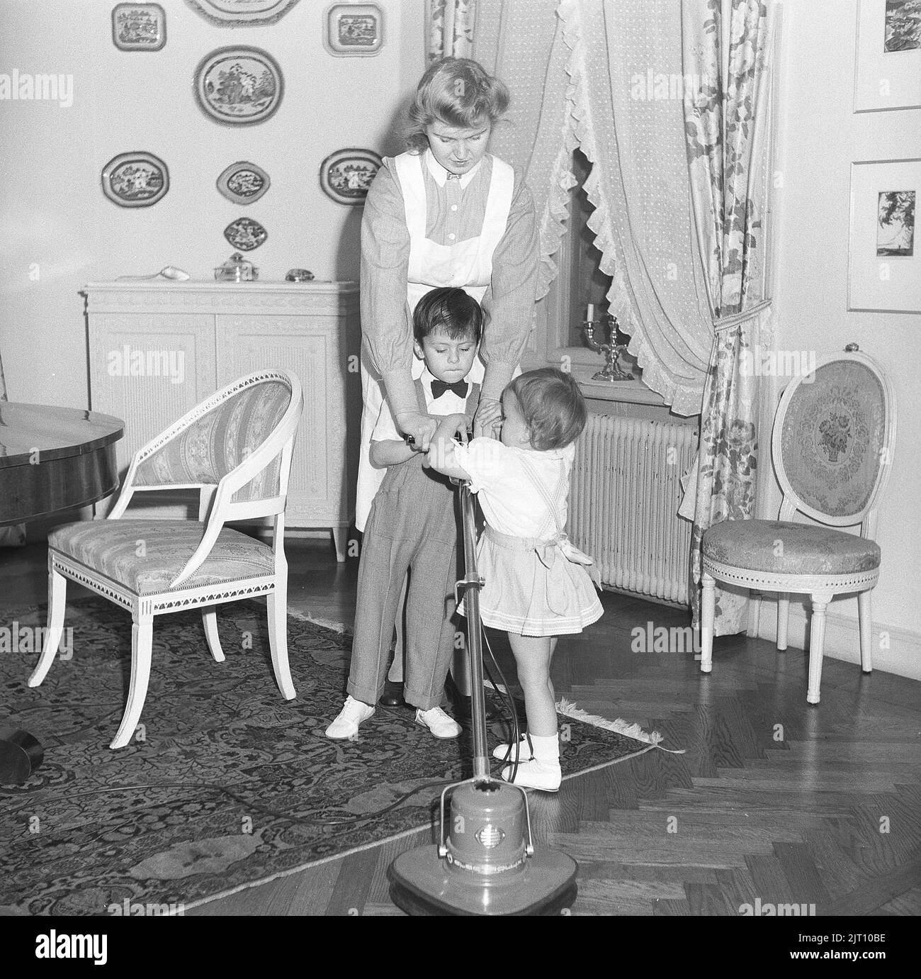 Zimmermädchen im Jahr 1940s. Eine junge Frau, die in einem Haus als Dienstmädchen arbeitet und durch das Aussehen davon auch das Kindermädchen, wie lässt sie spielen und die Maschine ausprobieren, die gemacht wird, um die Böden zu polieren. Schweden 1947 Kristoffersson Ref. X147-1 Stockfoto