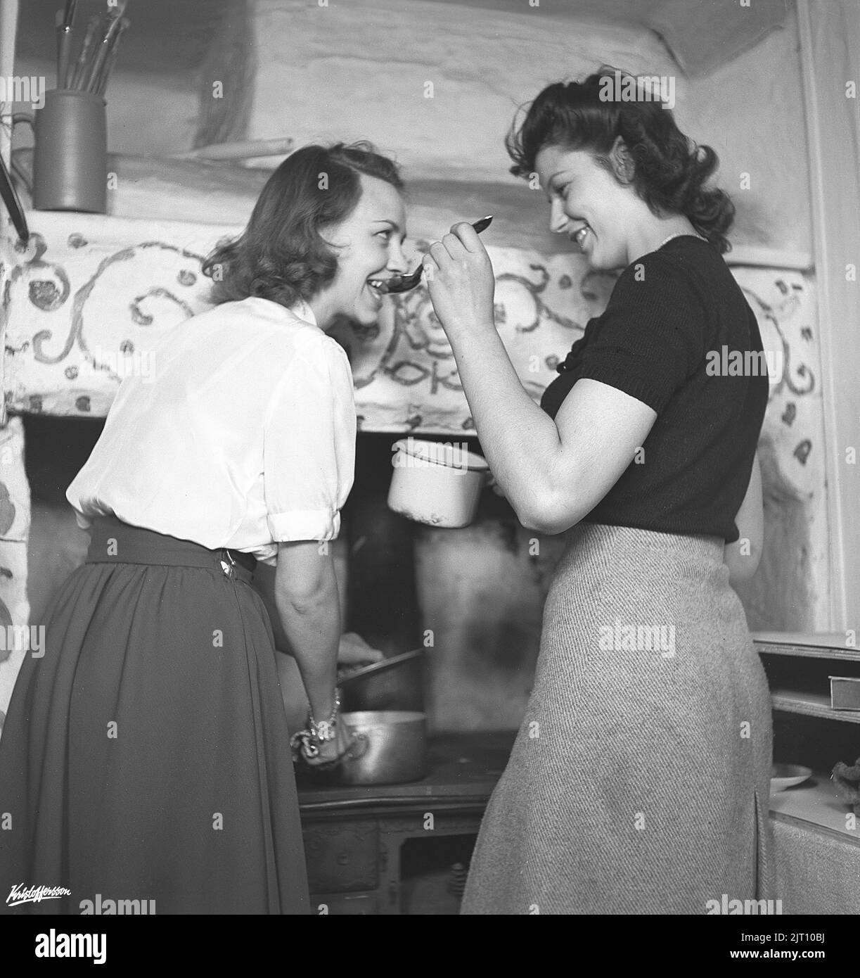 In der Küche 1940s. Interieur einer ländlichen Küche und zwei Frauen kochen zusammen, eine Verkostung aus dem Inhalt eines Eintopfes auf einem Löffel. Schweden 1945 Kristoffersson Ref. N143-5 Stockfoto