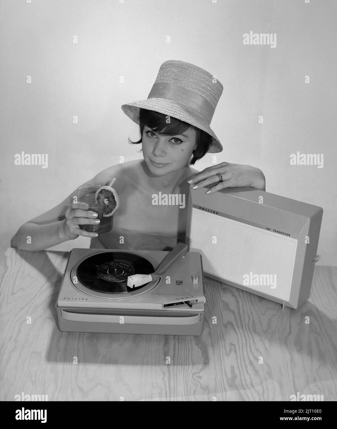 1960s Lifestyle. Eine junge Frau mit einem Philips Radio und einem Grammophon, wie es im Sommer aussehen könnte. Der Sommerhut und das kühle Trinkglas sind im Bild, um das richtige Sommergefühl zu bekommen. Schweden 1960s Foto Kristoffersson Ref 374A Stockfoto