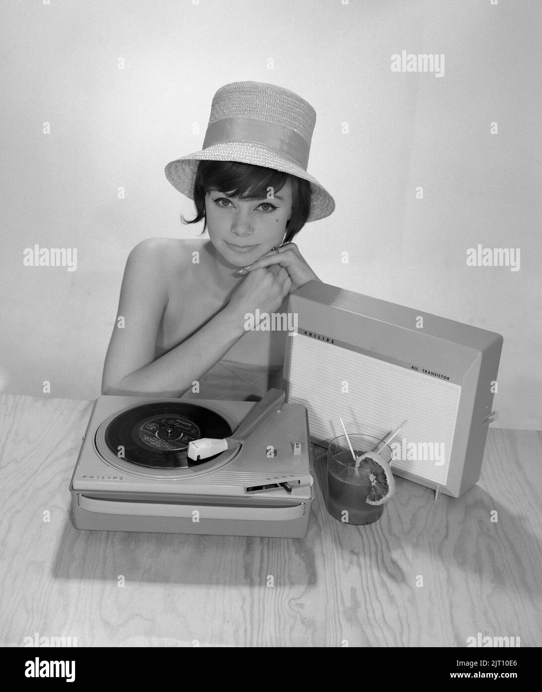 1960s Lifestyle. Eine junge Frau mit einem Philips Radio und einem Grammophon, wie es im Sommer aussehen könnte. Der Sommerhut und das kühle Trinkglas sind im Bild, um das richtige Sommergefühl zu bekommen. Schweden 1960s Foto Kristoffersson Ref 374A Stockfoto