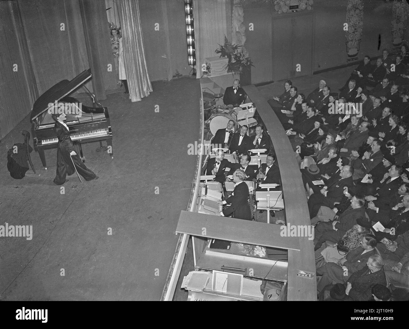 Charlie Chaplin ähnlich 1940s. Claire Felden, die professionelle Charlie Chaplin-Imitatorin, unterhält sich auf der Bühne des China Theatre in Stockholm. Sie trägt das typische Chaplin-Outfit, kane, Hut und Schnurrbart. Der oft nicht gesehene Graben zwischen Publikum und Bühne ist sichtbar, wo das Orchester spielt. Schweden 1940 Kristoffersson Ref. 53-7 Stockfoto