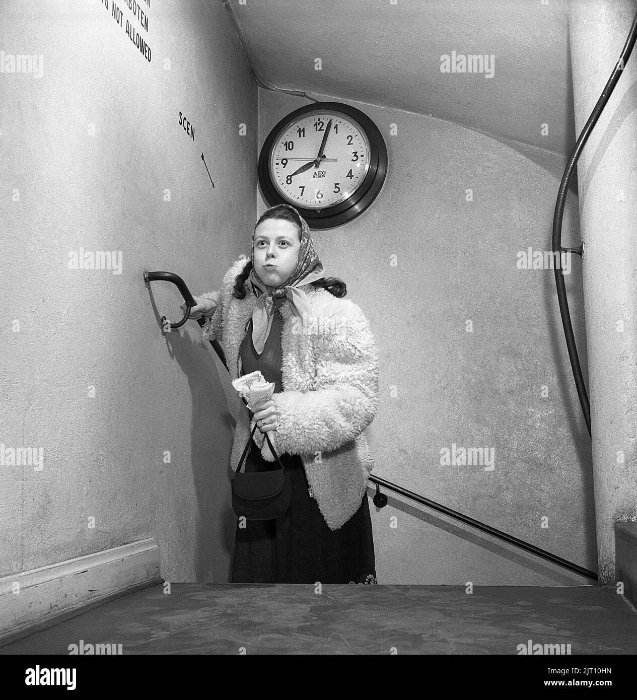 In der 1950s. Eine Frau ist sichtbar erschöpft, wenn sie die Treppe hinauf läuft, vielleicht ist sie ein paar Minuten zu spät für ihren Termin um acht Uhr, da die Uhr an der Wand zeigt, dass es ein paar Minuten vorbei ist. Schweden 1950 Kristoffersson Ref. AX7-1 Stockfoto