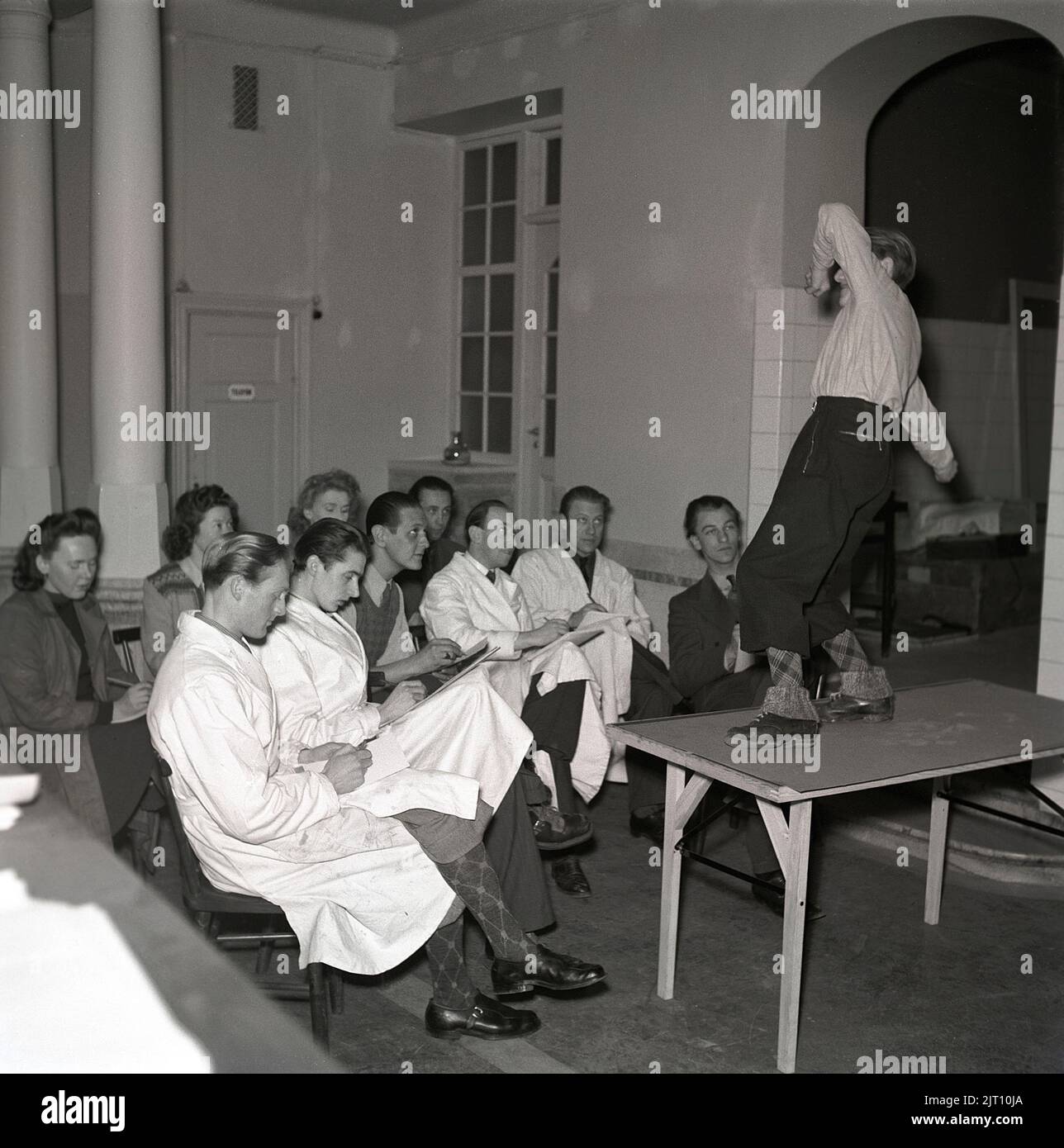 Kunstschule der 1940s. Eine Gruppe junger Männer und Frauen zeichnet das Bild des jungen Mannes, der vor ihnen auf einem Tisch steht und in einem dramatischen Herrenhaus posiert. Das männliche Modell ist in typischen 1940s Kleidern gekleidet. Möglicherweise ein Bild tacen während einer Kunstklasse. Schweden 1942 Kristoffersson Ref. A40-2 Stockfoto
