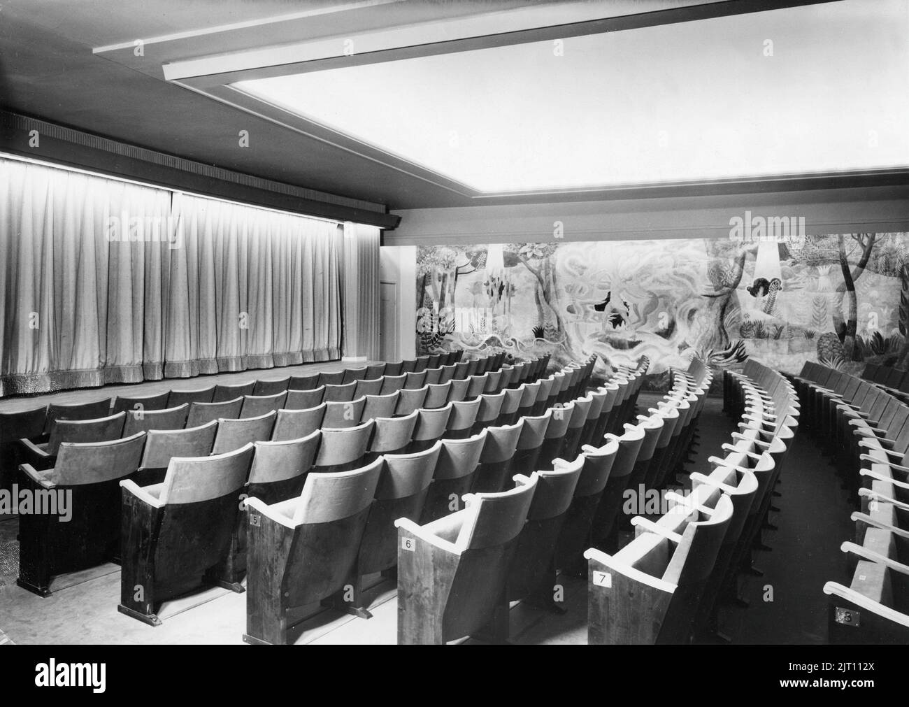 Bequeme Stühle. Ein Bild aus einem Kino mit leeren Sitzen. Die Sitzreihen sind nummeriert, sodass die Personen, die mit Tickets und Sitzplatzdetails kommen, ihren Platz im Theater finden können. Der Vorhang bedeckt die Filmleinwand. Die Wand ist dekoriert. Schweden 1950s Stockfoto