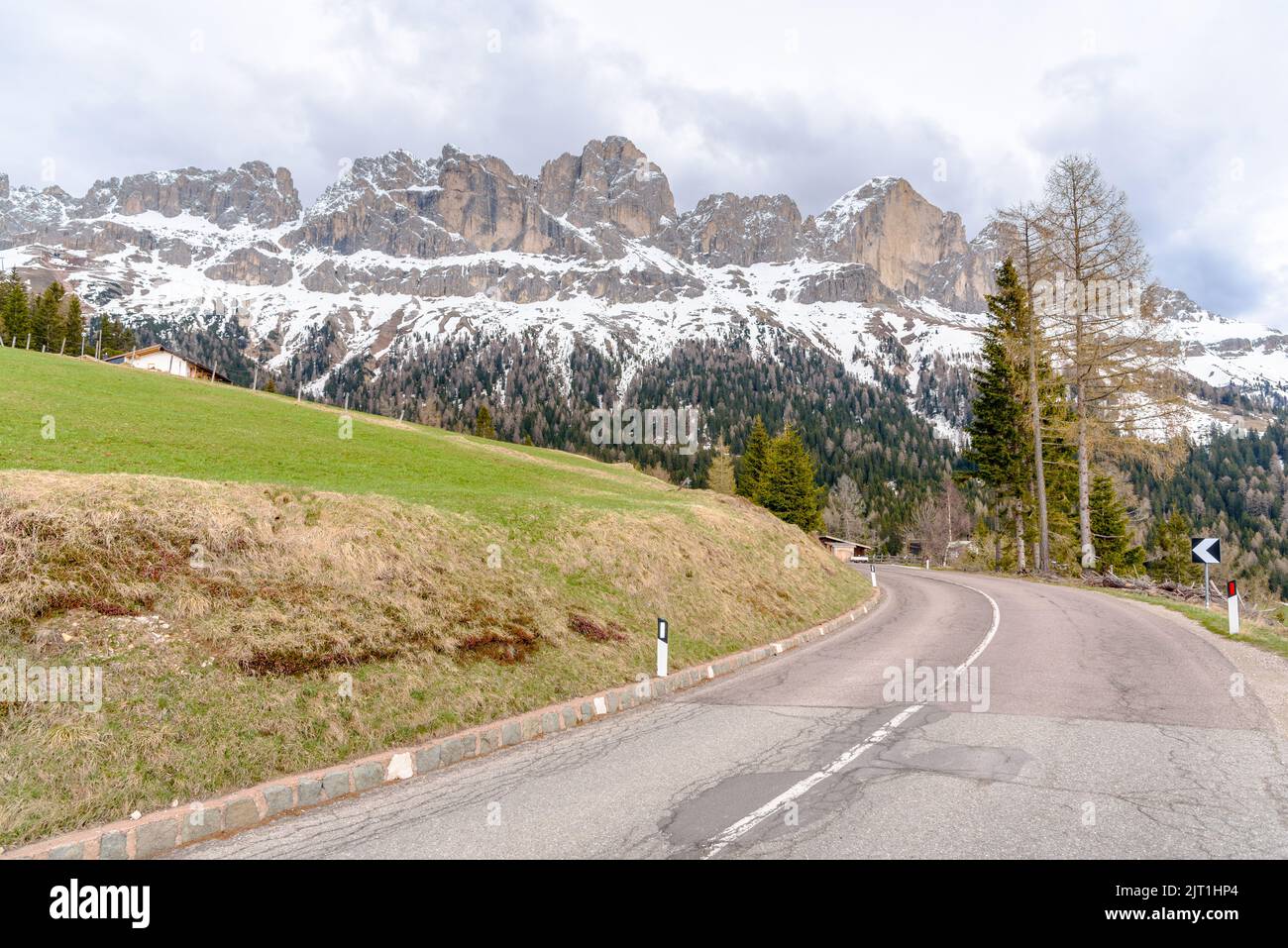 Kurve entlang einer Bergpassstraße, die am Fuße der schneebedeckten Gipfel in den Europäischen Alpen an einem bewölkten Frühlingstag verläuft Stockfoto