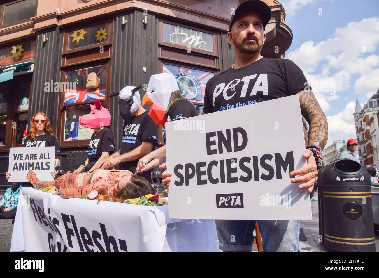 London, Großbritannien. 27. August 2022. Ein PETA-Protestler (People for the Ethical Treatment of Animals) hält ein Plakat mit dem Titel „Ende des Speziesismus“, während andere Aktivisten, die Tiermasken tragen, während der Proteste auf dem Leicester Square einen mit gefälschtem Blut bedeckten Aktivisten mit „dinen“. Die Aktion, die den Welttag für das Ende des Speziesismus markiert, ist Teil der laufenden Kampagne von PETA zur Beendigung des Speziesismus und zur Ermutigung der Menschen, vegan zu gehen. Kredit: SOPA Images Limited/Alamy Live Nachrichten Stockfoto