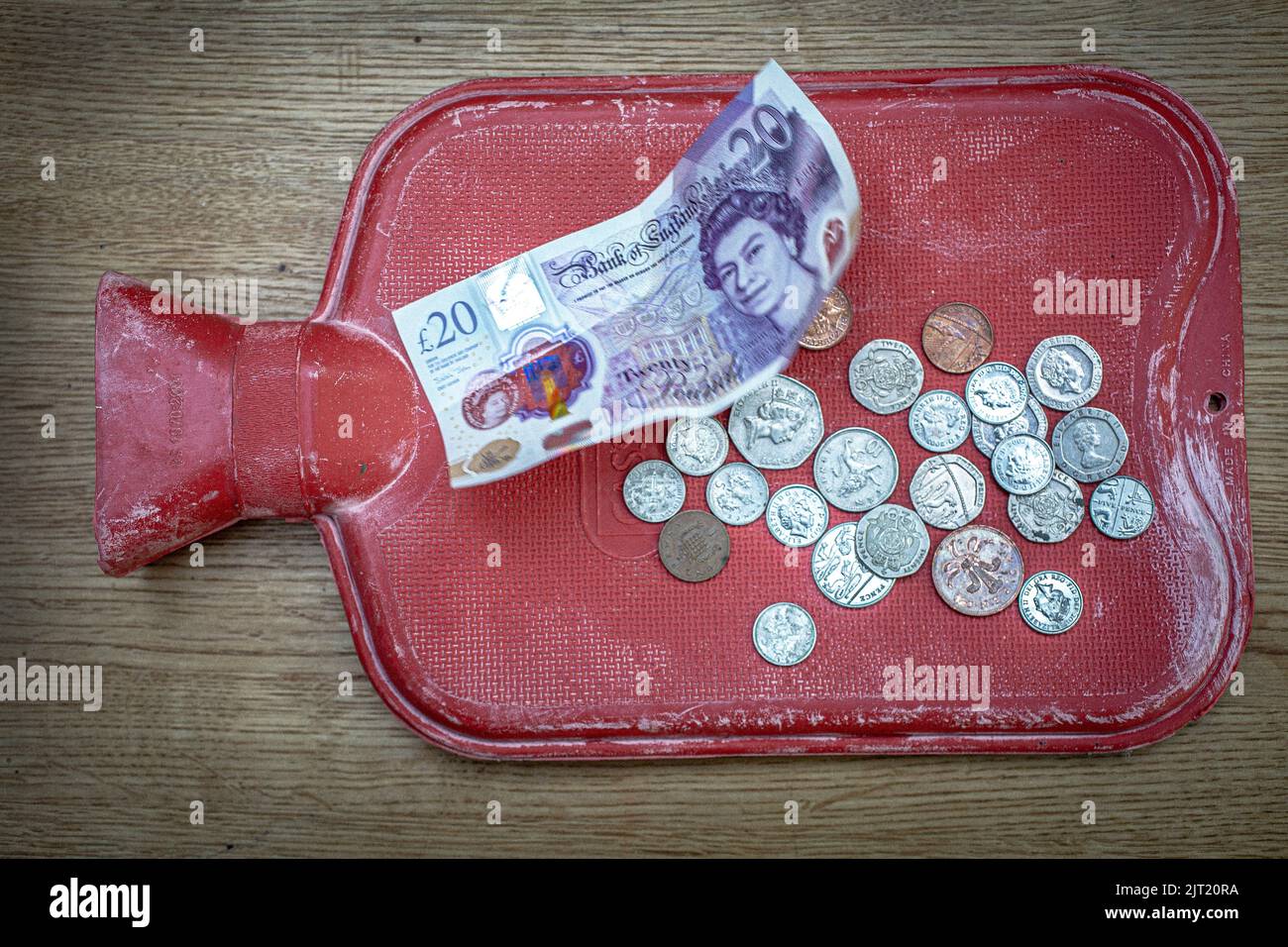 Nahaufnahme einer Heißwasserflasche und britischer £20-Note und Münzen als Treibstoffrechnung Rakete Stockfoto