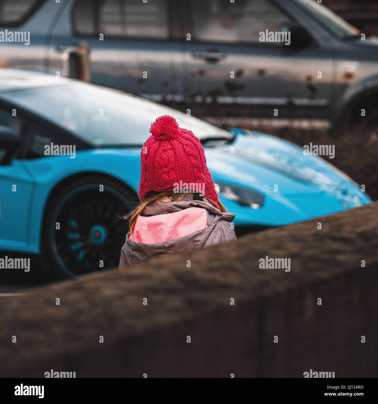 Ein kleines Mädchen mit rotem Hut vor einem blauen Sportwagen, Stadtleben in der Stadt Karlsruhe Stockfoto