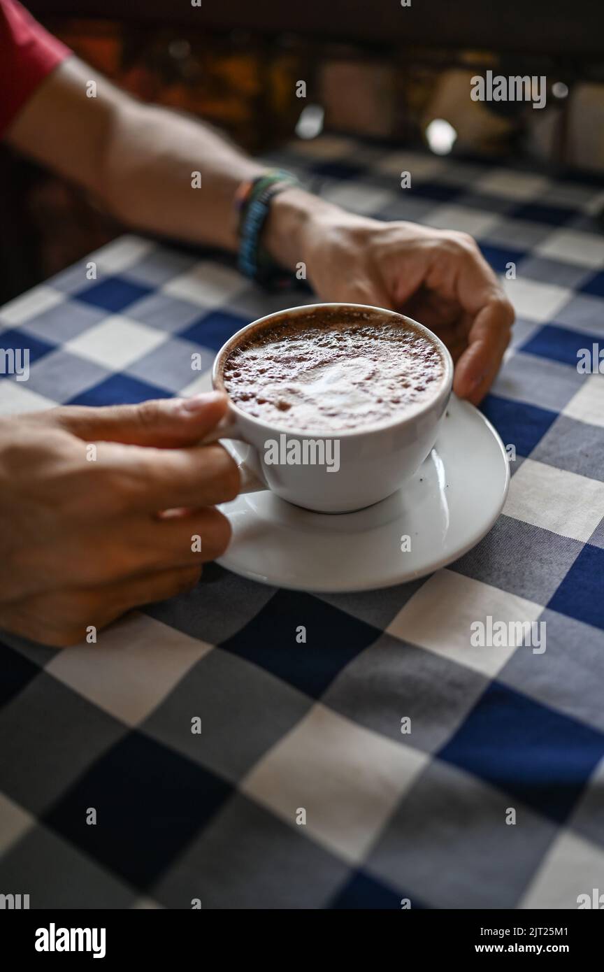 Hände eines Mannes, der eine Tasse heiße Schokolade auf dem Restauranttisch hält Stockfoto