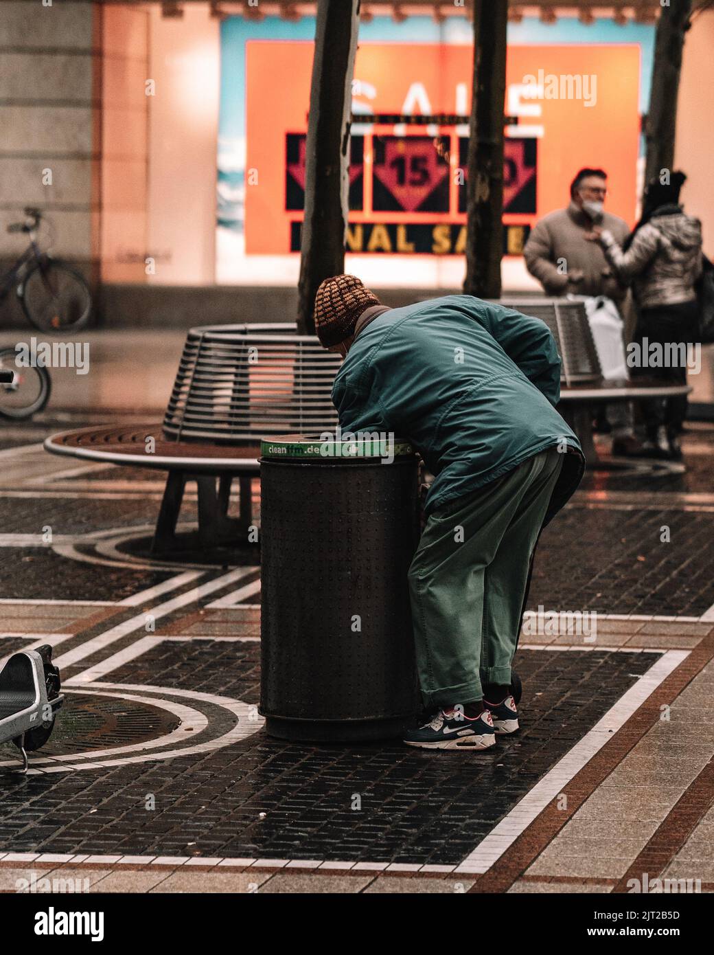 Ein urbanes Leben in der Stadt mit einer Person, die einen Mülleimer gräbt Stockfoto