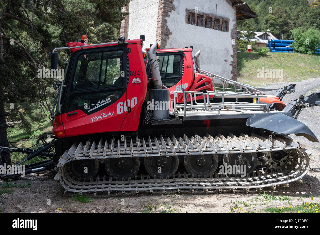 Ein roter PistenBully 600 W Pistengroomer parkte an einem sonnigen Tag in der Nähe eines grünen Baumes und eines Gebäudes Stockfoto